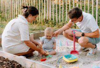 Gezin speelt in een zandbak bij Boszee - Glampingtenten West-Vlaanderen, omgeven door natuur.