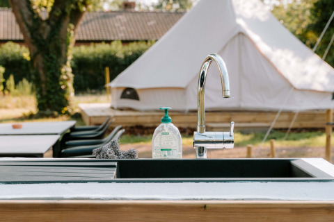 Évier extérieur avec savon et éponge, tente glamping en arrière-plan chez Boszee - Glampingtenten West-Vlaanderen.