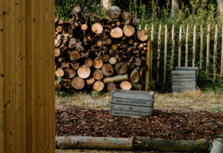 Gestapeld hout, omheining en houten kisten bij Boszee Glampingtenten West-Vlaanderen in de natuur.