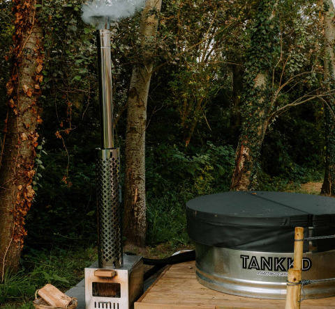 Outdoor wood-fired hot tub with smokestack and cover set on a deck in the woods at Boszee Glampingtenten West-Vlaanderen.