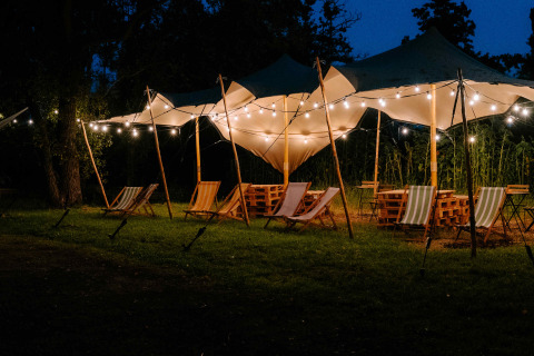 Espace glamping extérieur de nuit avec tentes, guirlandes lumineuses et chaises chez Boszee Glampingtenten.