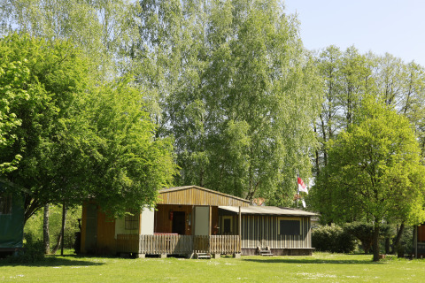 Hébergement glamping à Kano & Kamp Aqua Hema- Blokhutten Beieren, entouré d’arbres verts et de soleil.
