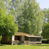 Glamping accommodation at Kano & Kamp Aqua Hema- Blokhutten Beieren, set amongst lush green trees and sunshine.