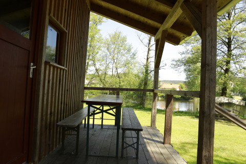 Houten veranda met bank en tafel bij Kano & Kamp Aqua Hema- Blokhutten Beieren, uitkijkend op het meer.