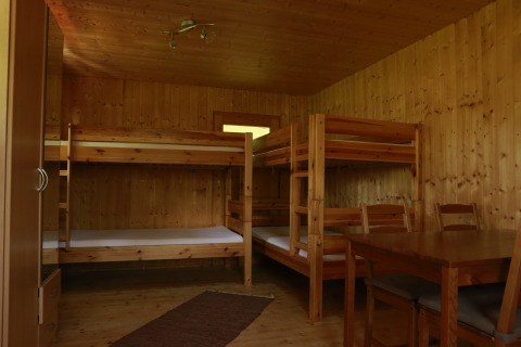 Casetta in legno con due letti a castello, tavolo da pranzo e sedie, glamping al Kano & Kamp Aqua Hema in Baviera.