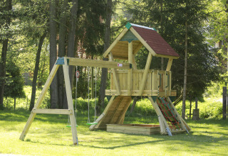 Wooden playground set with swings, climbing net and sandbox at Kano & Kamp Aqua Hema- Blokhutten Beieren.
