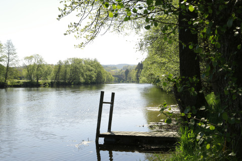 Muelle de madera junto al río rodeado de árboles en Kano & Kamp Aqua Hema- Blokhutten Beieren camping.