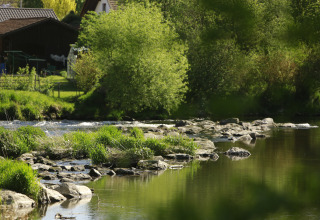 River with rocks and lush vegetation at Kano & Kamp Aqua Hema- Blokhutten Beieren glamping accommodation.