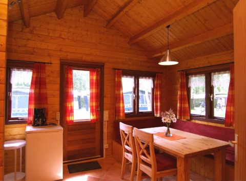 Houten interieur van glampingaccommodatie met eettafel, stoelen en rode gordijnen bij Eifelidyll camping.