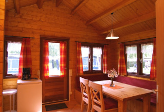 Holzinterieur einer Glamping-Unterkunft mit Esstisch, Stühlen und roten Vorhängen, Eifelidyll Camping.