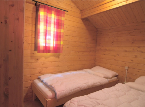 Træværelse med to senge og farverigt gardin i glamping-indkvarteringen Eifelidyll, Rheinland-Pfalz.