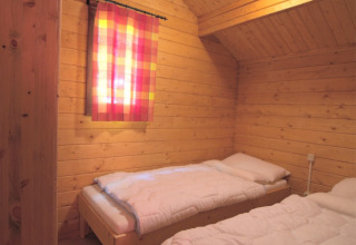 Holzzimmer mit zwei Betten und buntem Vorhang in der Glamping-Unterkunft Eifelidyll, Rheinland-Pfalz.