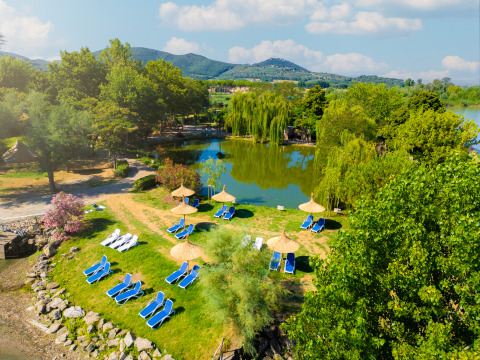 Vista aerea del Trasimeno Glamping Resort con lettini, ombrelloni, lago e natura verde rigogliosa.