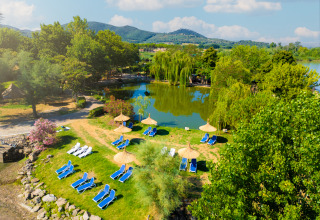 Vue aérienne du Trasimeno Glamping Resort avec transats, parasols, lac et paysage verdoyant.