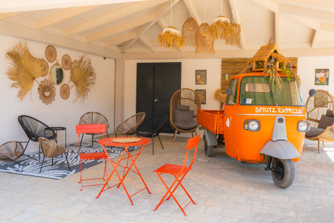 Colorido lounge exterior en Trasimeno Glamping Resort con camioneta Spritz Express y asientos modernos.