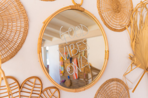 Specchio tondo con scritta 'GOOD VIBES ONLY' al Trasimeno Glamping Resort tra decorazioni in vimini.