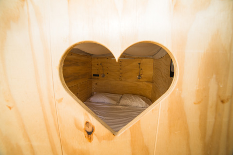 Vista attraverso un’apertura a forma di cuore su un lodge in legno al Trasimeno Glamping Resort in Umbria.