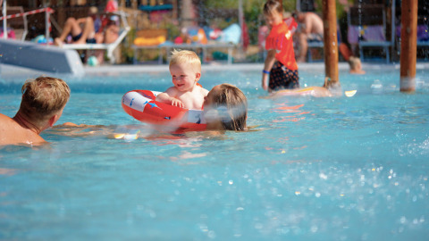 Familia disfruta de la piscina en Trasimeno Glamping Resort mientras un niño pequeño juega en un flotador.