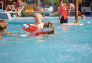Family enjoys the pool at Trasimeno Glamping Resort as a toddler plays with a float under the summer sun.