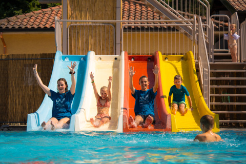 Famiglie si divertono sugli scivoli d’acqua al Trasimeno Glamping Resort, bambini e adulti felici in piscina.