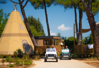 Børn leger i mini-jeeps foran et tipitelt og hytter på Trasimeno Glamping Resort i Italien.