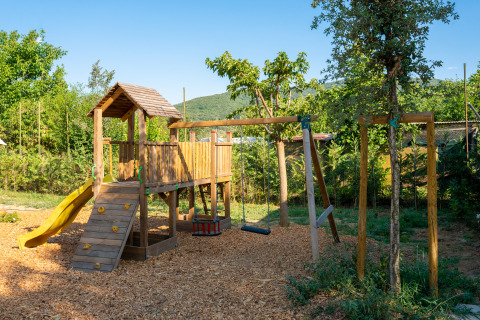 Holzspielplatz mit Rutsche und Schaukeln in grüner Umgebung im Trasimeno Glamping Resort, Italien.