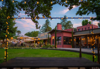Terrasse extérieure du Trasimeno Glamping Resort avec guirlandes lumineuses, pelouse verte et tables au crépuscule.