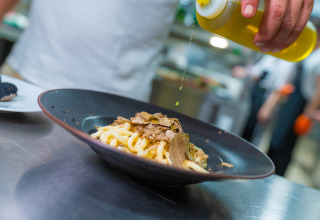Chef che versa olio su pasta fresca con tartufo in un ristorante vicino al Trasimeno Glamping Resort in Umbria.