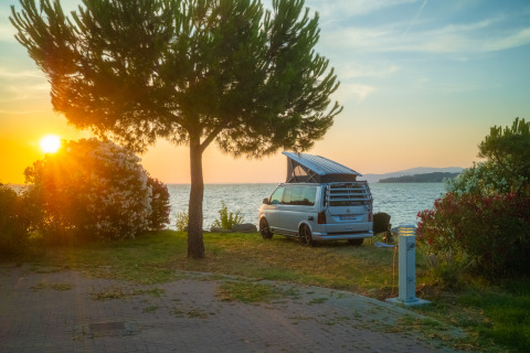 Solnedgang ved søen ved Trasimeno Glamping Resort med autocamper og træer, ideel glamping i Italien.