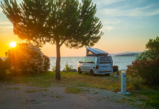 Sonnenuntergang am See beim Trasimeno Glamping Resort, Campervan und Bäume, perfekte Glamping-Erfahrung.
