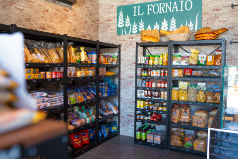 Interieur van een bakkerijwinkel 'Il Fornaio' met volle schappen brood, pasta en diverse levensmiddelen.