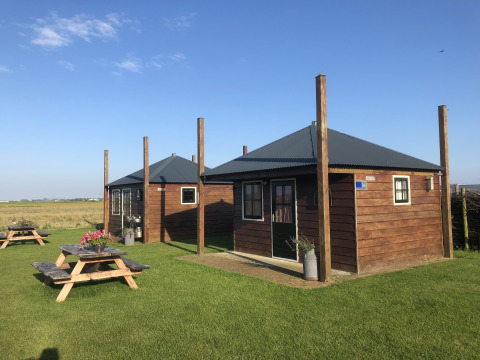 Zwei Holzhütten mit Picknicktischen auf einer Wiese bei Camping Duinzoomhoeve – Hooiberghut Glamping Noord-Holland.