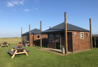 Twee houten huisjes met picknicktafels op grasveld bij Camping Duinzoomhoeve – Hooiberghut glamping Noord-Holland.