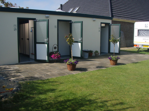 Edificio sanitario al aire libre en Camping Duinzoomhoeve – Hooiberghut glamping Noord-Holland, con flores.