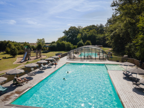 Outdoor-Pool und Spielplatz im Village Huttopia Senonches - Glamping Val de Loire inmitten grüner Natur.