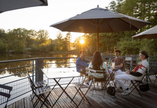 Quattro persone si rilassano su una terrazza sul lago a Village Huttopia Senonches - Glamping Val de Loire.