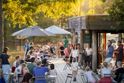 Personas disfrutando junto a un lago y música en vivo en Village Huttopia Senonches - Glamping Val de Loire.