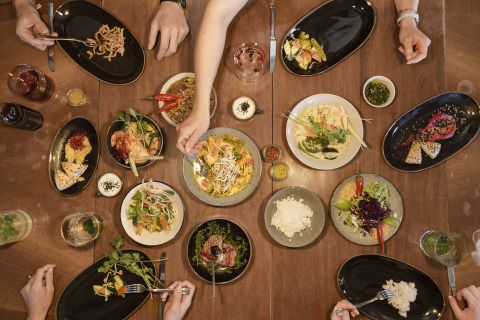 People share a colorful meal at a table in Adventure Camp Schnitzmühle Tiny House Beierse Woud in a glamping setting.