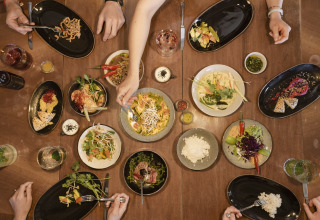 People share a colorful meal at a table in Adventure Camp Schnitzmühle Tiny House Beierse Woud in a glamping setting.