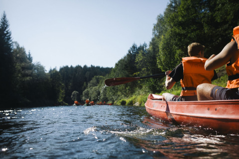 Menschen mit Rettungswesten paddeln im Kanu auf einem Fluss, umgeben vom Wald, nahe Adventure Camp Schnitzmühle.