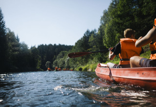 Personas con chalecos salvavidas naranjas remando en canoa en un río cerca de Adventure Camp Schnitzmühle, Baviera.