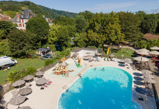 Luxus-Camping Huttopia Beaulieu sur Dordogne mit Pool, Liegen und Spielplatz in grüner Umgebung.