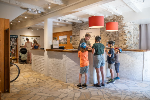 Reception area at Huttopia Beaulieu sur Dordogne with families and children wearing bike helmets for glamping.