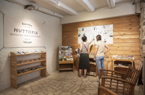 Dos personas consultan un mapa y folletos en la recepción de Huttopia Beaulieu sur Dordogne glamping site.