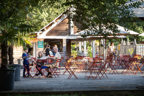 Buitenterras bij Huttopia Beaulieu sur Dordogne met gezinnen, kinderen, bomen en rode tafels in de zon.
