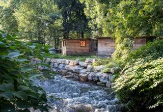 Cabine in legno vicino a un fiume da Huttopia Beaulieu sur Dordogne – Glamping Dordogne, circondate da alberi.