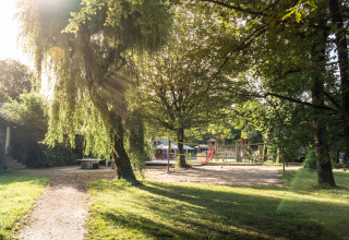 Parque infantil bajo la luz del sol y rodeado de árboles en Huttopia Beaulieu sur Dordogne – Glamping Dordogne.