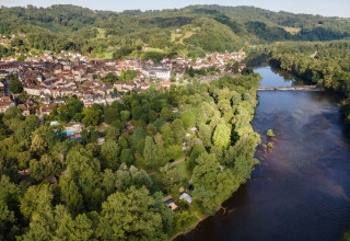 Luftfoto af Huttopia Beaulieu sur Dordogne glamping og camping omgivet af grønne træer ved en flod.