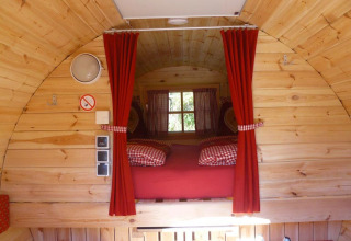 Interieur van een glamping wijnvat in Baden-Württemberg met houten wanden, rode gordijnen en knus bed.