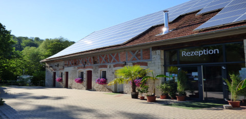 Eingangsbereich von Camping Schwabenmühle mit Solarpaneelen auf dem Dach und Blumendekoration.